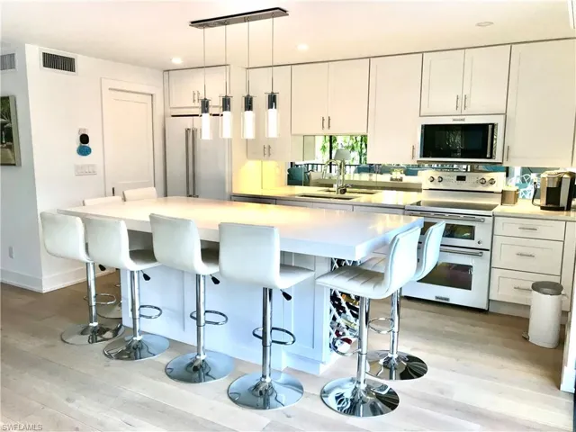 Kitchen featuring range with two ovens, a sink, white cabinets, high end fridge, and a kitchen bar
