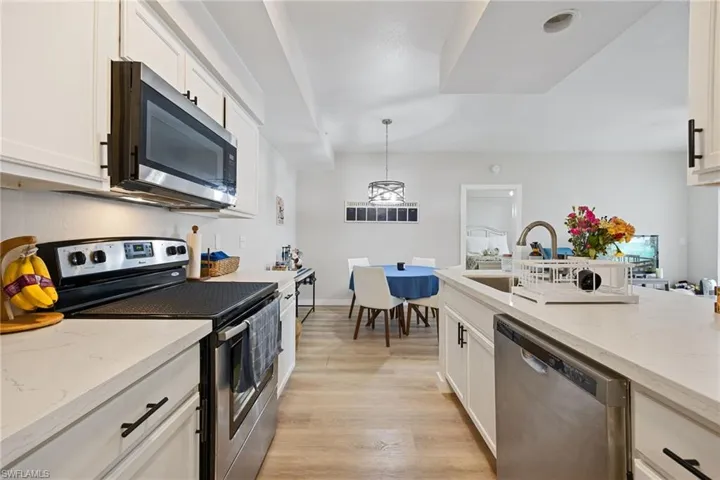 Kitchen featuring stainless steel appliances, light stone counters, white cabinets, and light wood-style floors