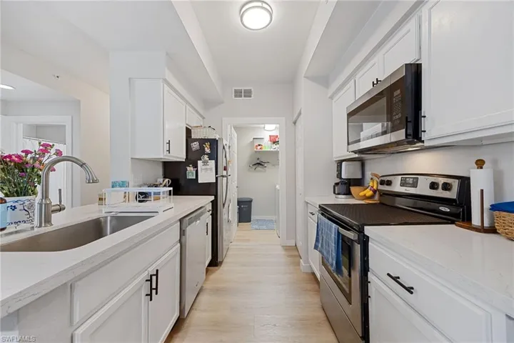 Kitchen with stainless steel appliances, light stone countertops, white cabinetry, and light wood-type flooring