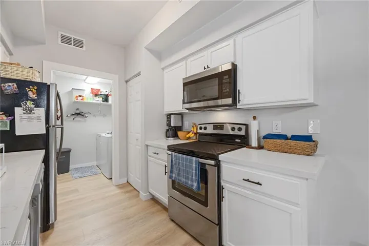 Kitchen with stainless steel appliances, white cabinetry, light wood-style flooring, and light stone counters