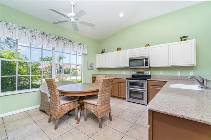 Kitchen featuring stainless steel appliances, light stone countertops, light tile patterned floors, lofted ceiling, and a ceiling fan