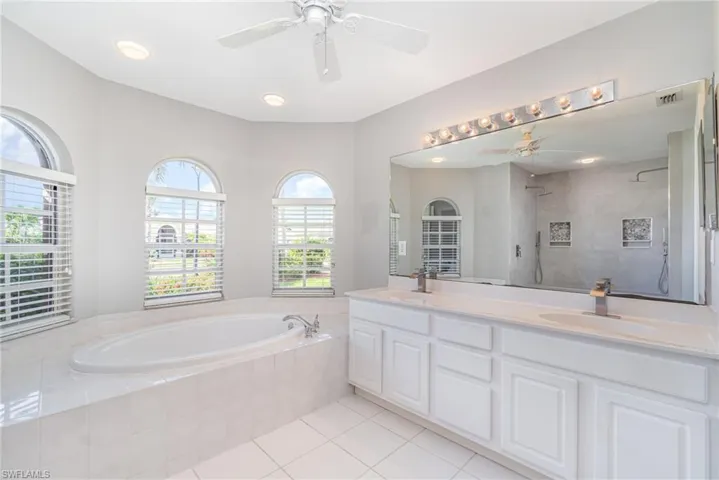 Bathroom featuring a garden tub, walk in shower, double vanity, light tile patterned floors, and a ceiling fan