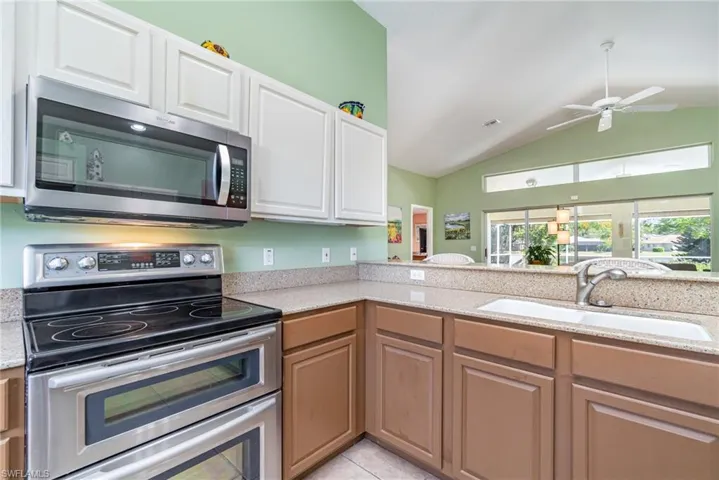 Kitchen with stainless steel appliances, light stone counters, ceiling fan, vaulted ceiling, and light tile patterned flooring