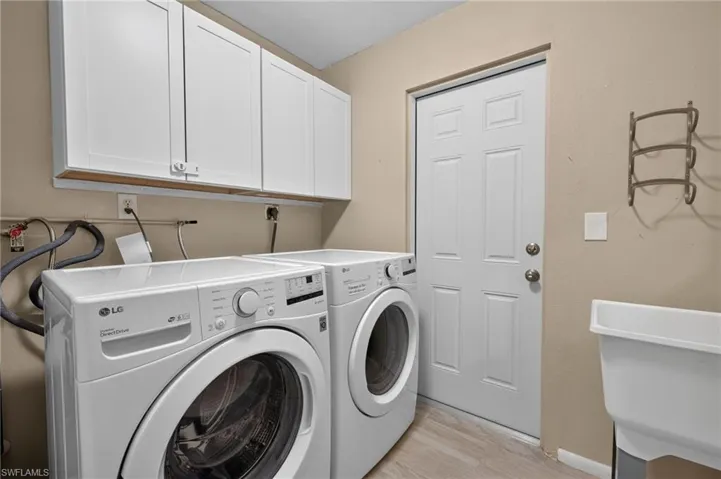 Dedicated laundry area featuring overhead white shaker-style cabinetry, a utilitarian sink, and light tile flooring
