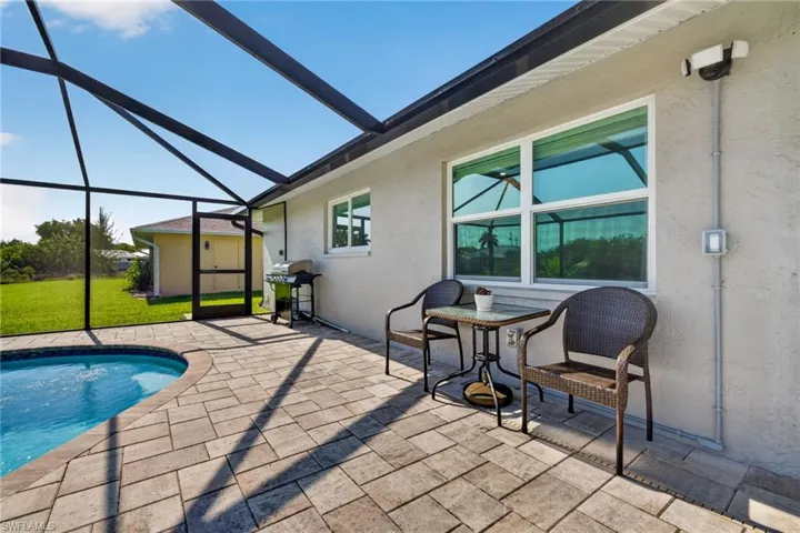 Screened lanai featuring a curved swimming pool, paver deck, and stucco exterior