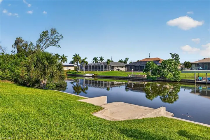 Waterfront property featuring a concrete seawall, lush green lawn, tropical landscaping, and a direct canal frontage