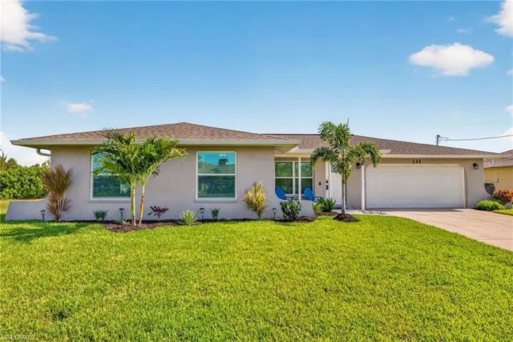 Single-story stucco residence featuring a two-car garage, mature landscaping, and an inviting front lawn