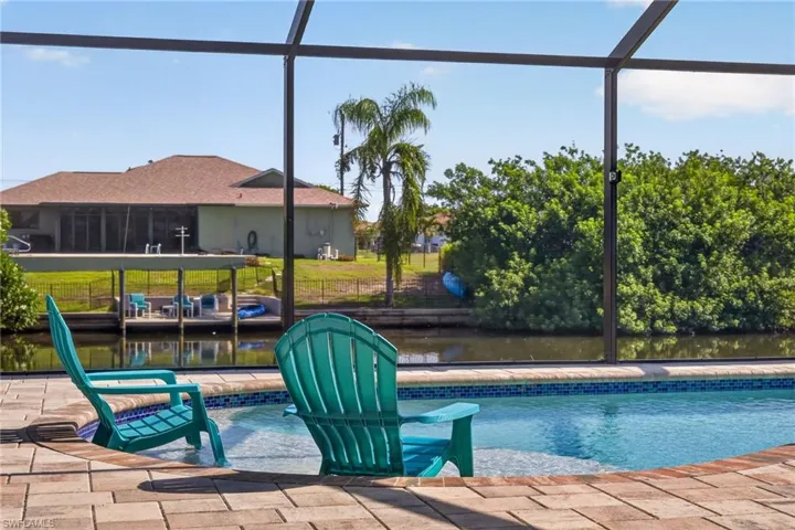 Screened-in pool area featuring a curved swimming pool with integrated seating, brick paver decking, and a mosaic tile waterline