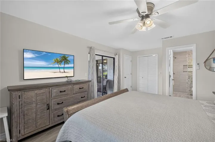 Bedroom featuring wood-finish flooring, a ceiling fan with integrated lighting, louvered closet doors, and access to an ensuite bathroom with a tiled shower