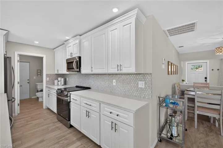 Kitchen featuring white shaker cabinetry, light-toned countertops, a mosaic tile backsplash, stainless steel appliances, and plank tile flooring