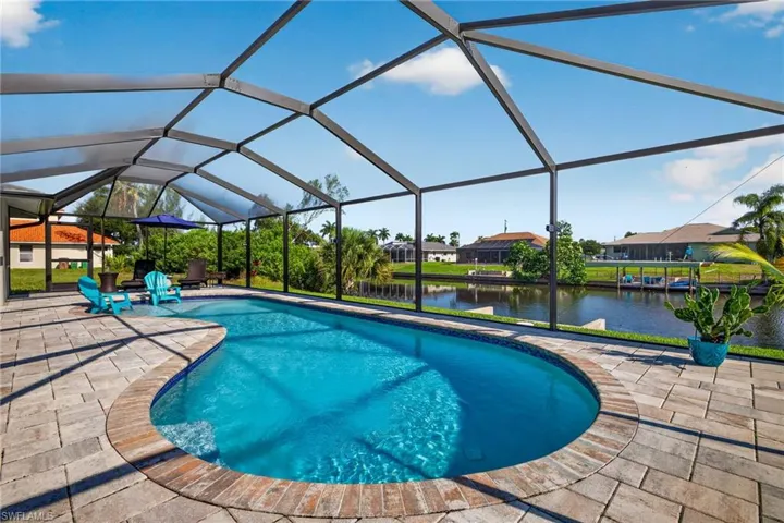 Screened enclosure featuring a freeform swimming pool, paver patio, brick coping, and a canal backdrop