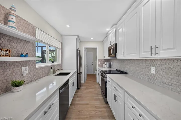 Galley kitchen featuring white cabinetry, light-toned countertops, a light hexagonal tile backsplash, stainless steel appliances, and tile flooring