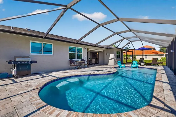 Screened-in outdoor living space featuring a freeform swimming pool with a tiled edge, paver patio, and stucco exterior