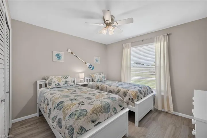 Light-filled room featuring two white-framed beds, tile flooring, and neutral wall tones