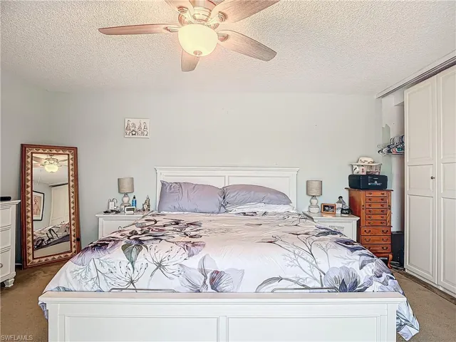 Bedroom featuring light carpet, ceiling fan, and a textured ceiling