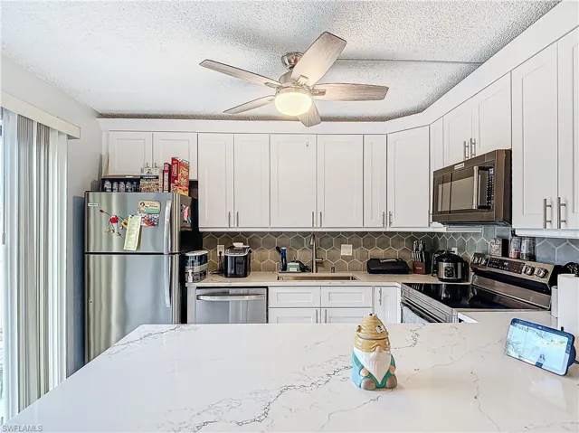 Kitchen featuring decorative backsplash, ceiling fan, stainless appliances, white cabinetry, and a deep sink
