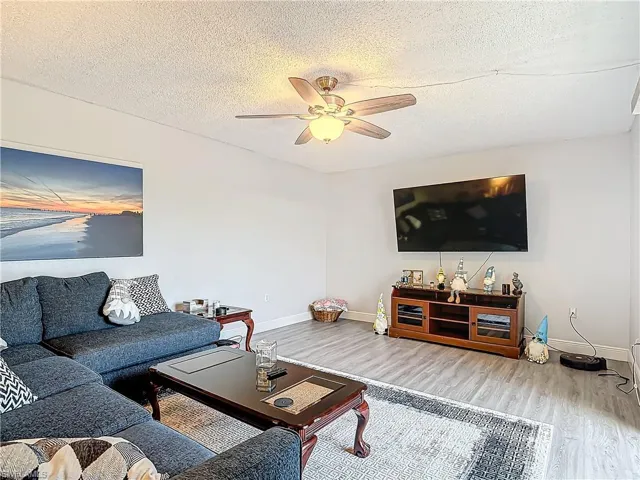 Living room with a textured ceiling, ceiling fan, and wood finished floors