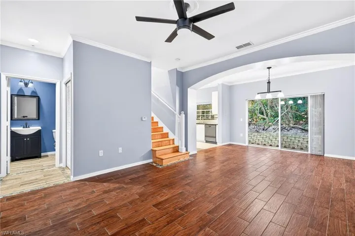 Unfurnished living room featuring wood finish floors, ornamental molding, stairs, ceiling fan, and arched walkways