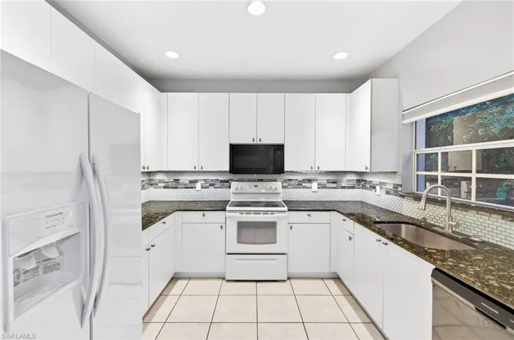 Kitchen featuring white appliances, dark stone counters, white cabinets, decorative backsplash, and recessed lighting