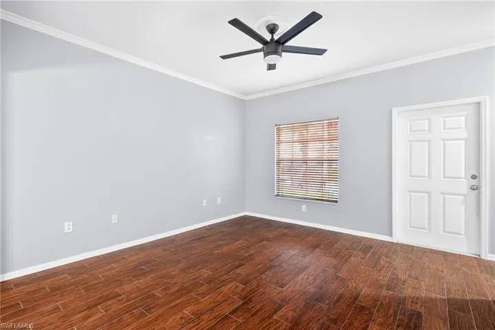 Empty room featuring crown molding, dark wood-style floors, and ceiling fan