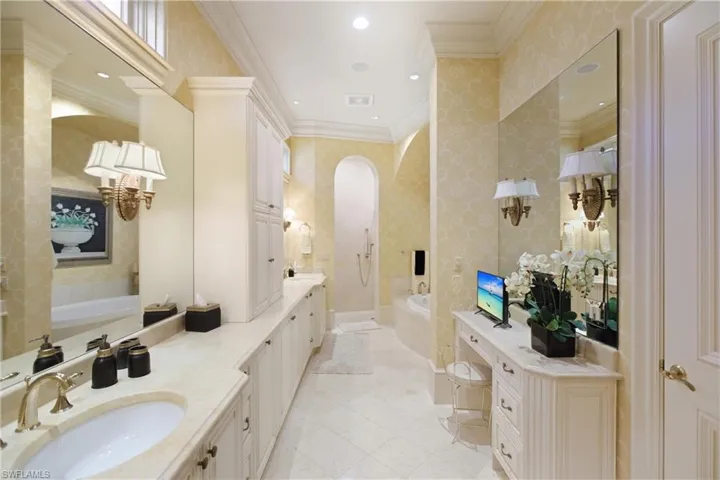 Bathroom with a bath, double vanity, wallpapered walls, crown molding, and light tile patterned flooring
