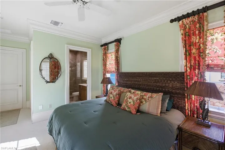 Carpeted bedroom featuring ensuite bath, ornamental molding, and ceiling fan