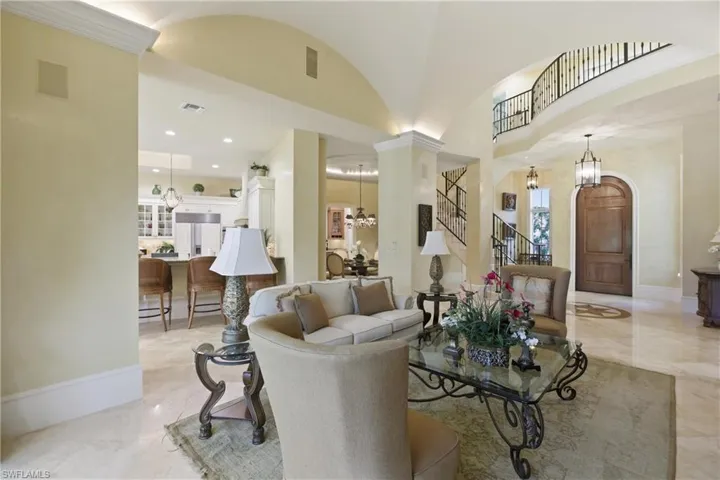 Living area featuring stairway, light marble finish flooring, a chandelier, vaulted ceiling, and arched walkways