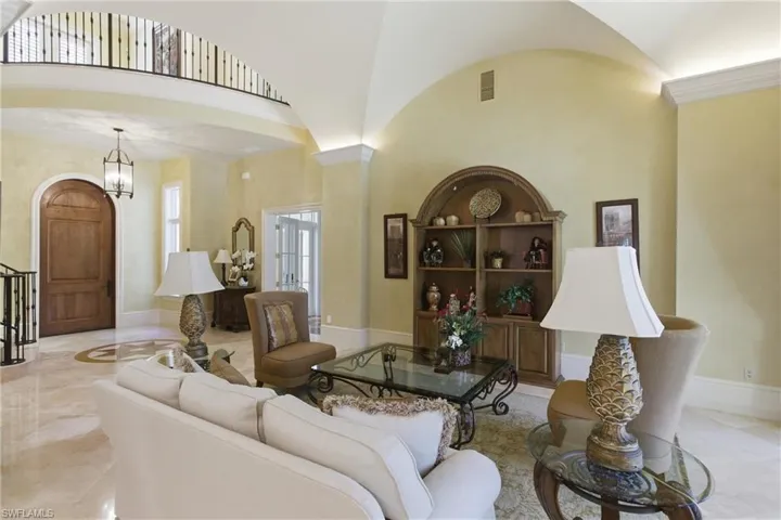 Living room featuring built in shelves, high vaulted ceiling, light marble finish flooring, and decorative columns