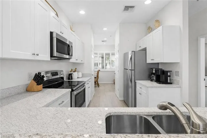 Virtual staged kitchen with stainless steel appliances, white cabinets, light stone counters, and recessed lighting