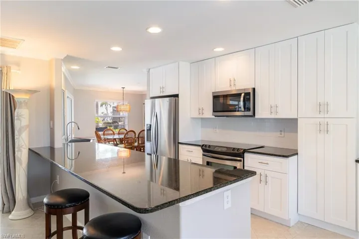 Kitchen featuring ornamental molding, appliances with stainless steel finishes, white cabinets, and a kitchen bar