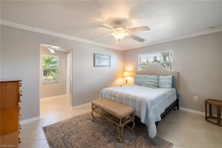 Tiled bedroom with multiple windows, ceiling fan, and ornamental molding