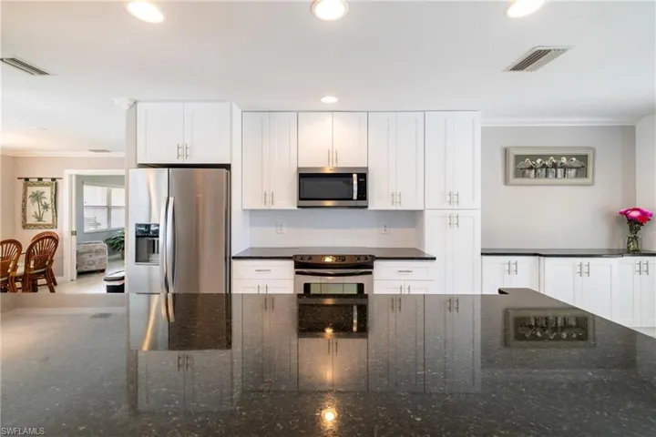 Kitchen featuring appliances with stainless steel finishes, decorative backsplash, ornamental molding, white cabinetry, and dark stone countertops