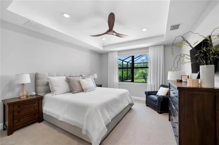 Bedroom with ceiling fan, light carpet, and a tray ceiling
