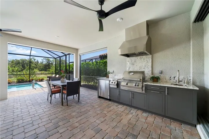 Kitchen with ceiling fan, wall chimney range hood, sink, fridge, and light stone countertops