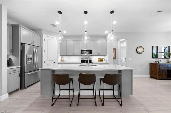 Kitchen featuring stainless steel appliances, decorative light fixtures, backsplash, and a center island with sink