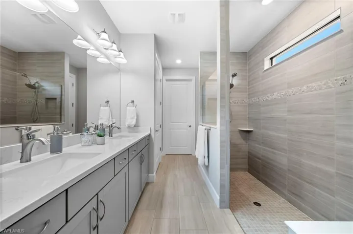 Bathroom with tiled shower, tile patterned flooring, and double sink vanity
