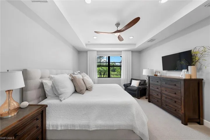Carpeted bedroom featuring ceiling fan and a tray ceiling