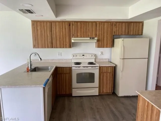Kitchen featuring white appliances, brown cabinetry, dark wood-type flooring, and light countertops