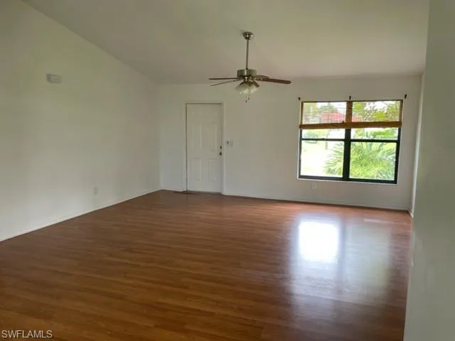 Empty room featuring dark wood-style flooring, a ceiling fan, and lofted ceiling