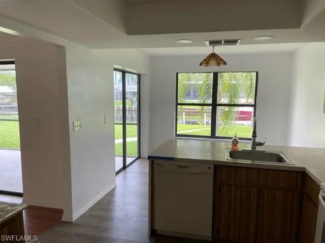 Kitchen featuring white dishwasher, dark wood-type flooring, brown cabinets, light countertops, and recessed lighting