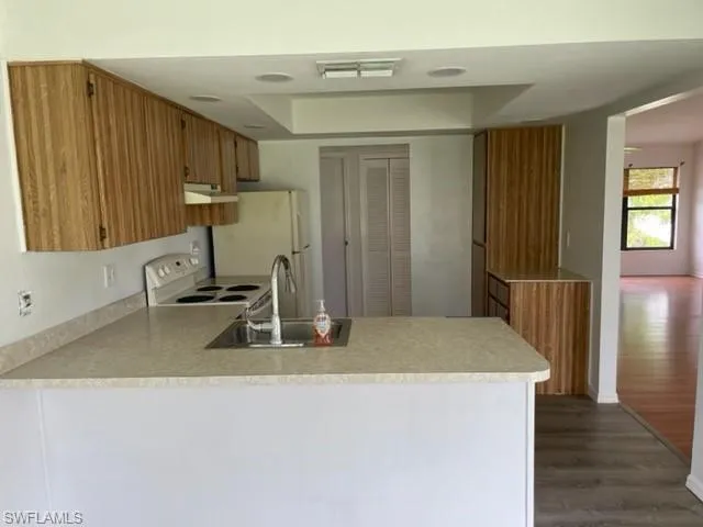 Kitchen featuring brown cabinetry, light countertops, a tray ceiling, a peninsula, and dark wood finished floors