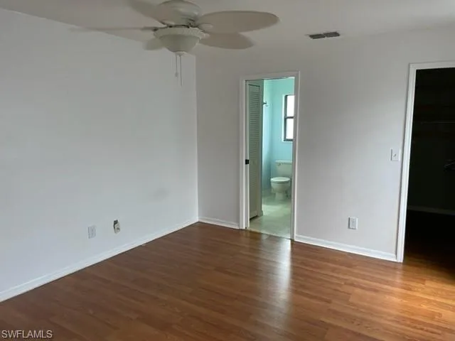 Unfurnished bedroom featuring a walk in closet, dark wood finished floors, and a ceiling fan