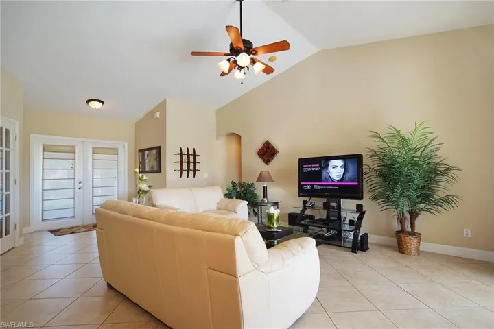 Living area with light tile patterned floors, vaulted ceiling, a ceiling fan, and arched walkways