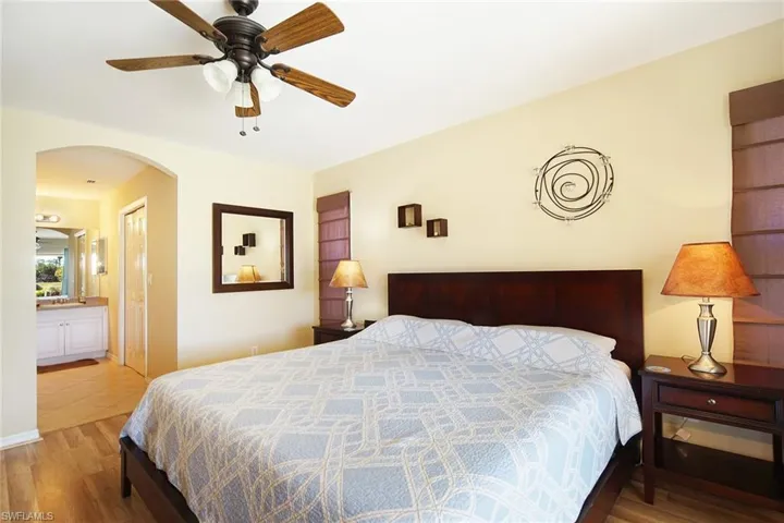 Bedroom with arched walkways, ensuite bathroom, a ceiling fan, and wood finished floors