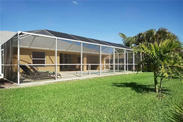 Back of house featuring a lawn, a patio area, an outdoor pool, and a lanai