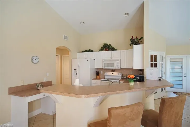 Kitchen featuring light tile patterned floors, white appliances, a peninsula, high vaulted ceiling, and arched walkways