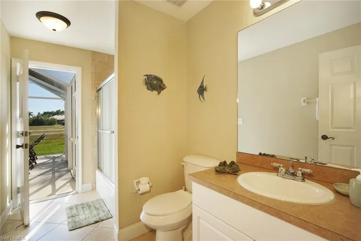 Bathroom featuring toilet, combined bath / shower with glass door, visible vents, tile patterned flooring, and vanity