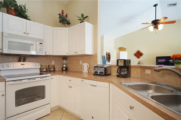 Kitchen featuring a sink, white appliances, tasteful backsplash, visible vents, and a ceiling fan