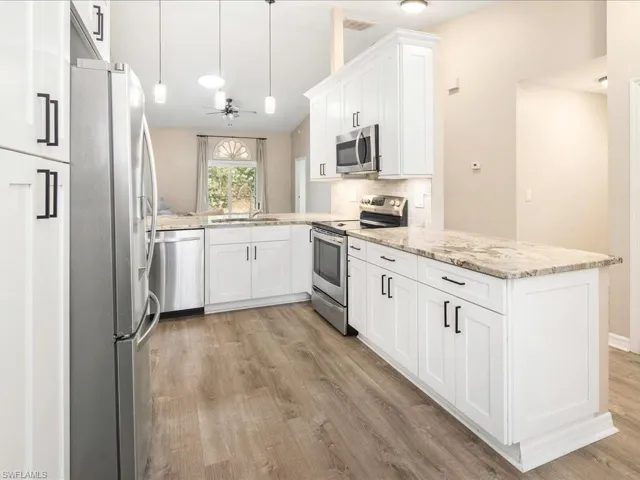 Kitchen with light stone countertops, a sink, light wood-style flooring, a peninsula, and appliances with stainless steel finishes