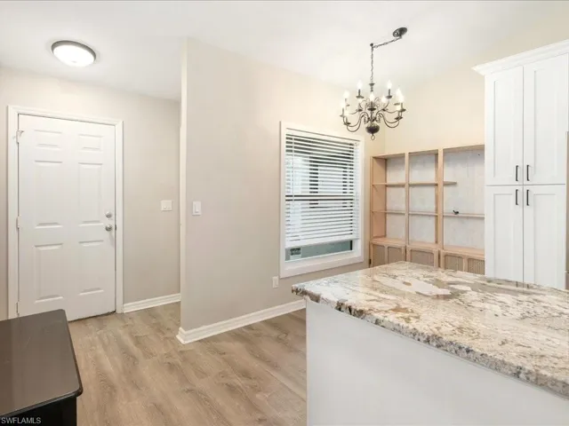 Kitchen featuring light wood-type flooring, white cabinets, light stone countertops, and an inviting chandelier